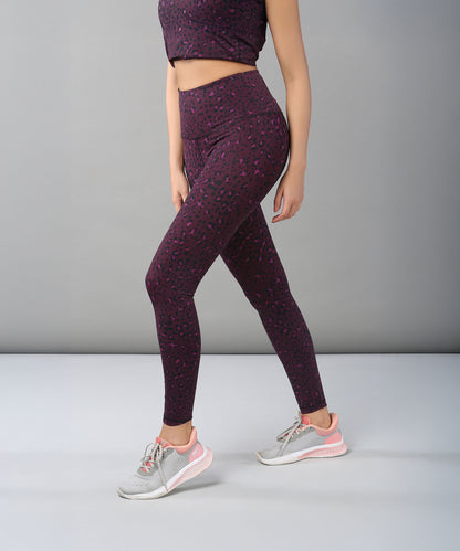 A woman wearing Pink Animal Print Leggings and gray sneakers stands against a plain gray background.