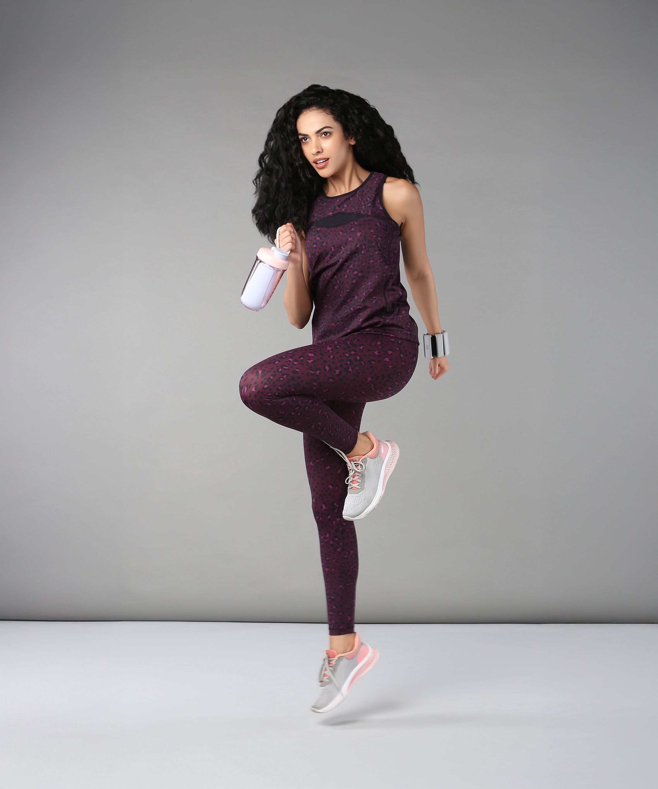 A woman wearing Pink Animal Print Leggings poses on one leg with a shaker bottle against a plain gray background.
