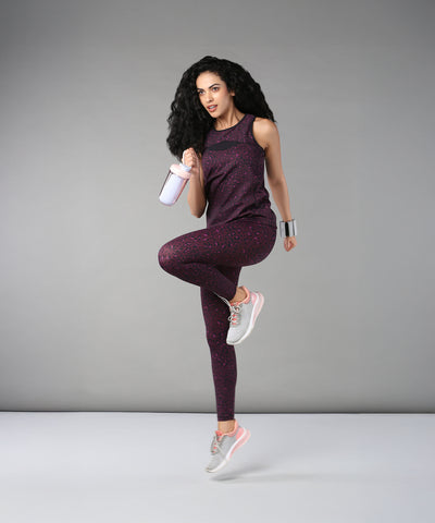 A woman wearing Pink Animal Print Leggings poses on one leg with a shaker bottle against a plain gray background.