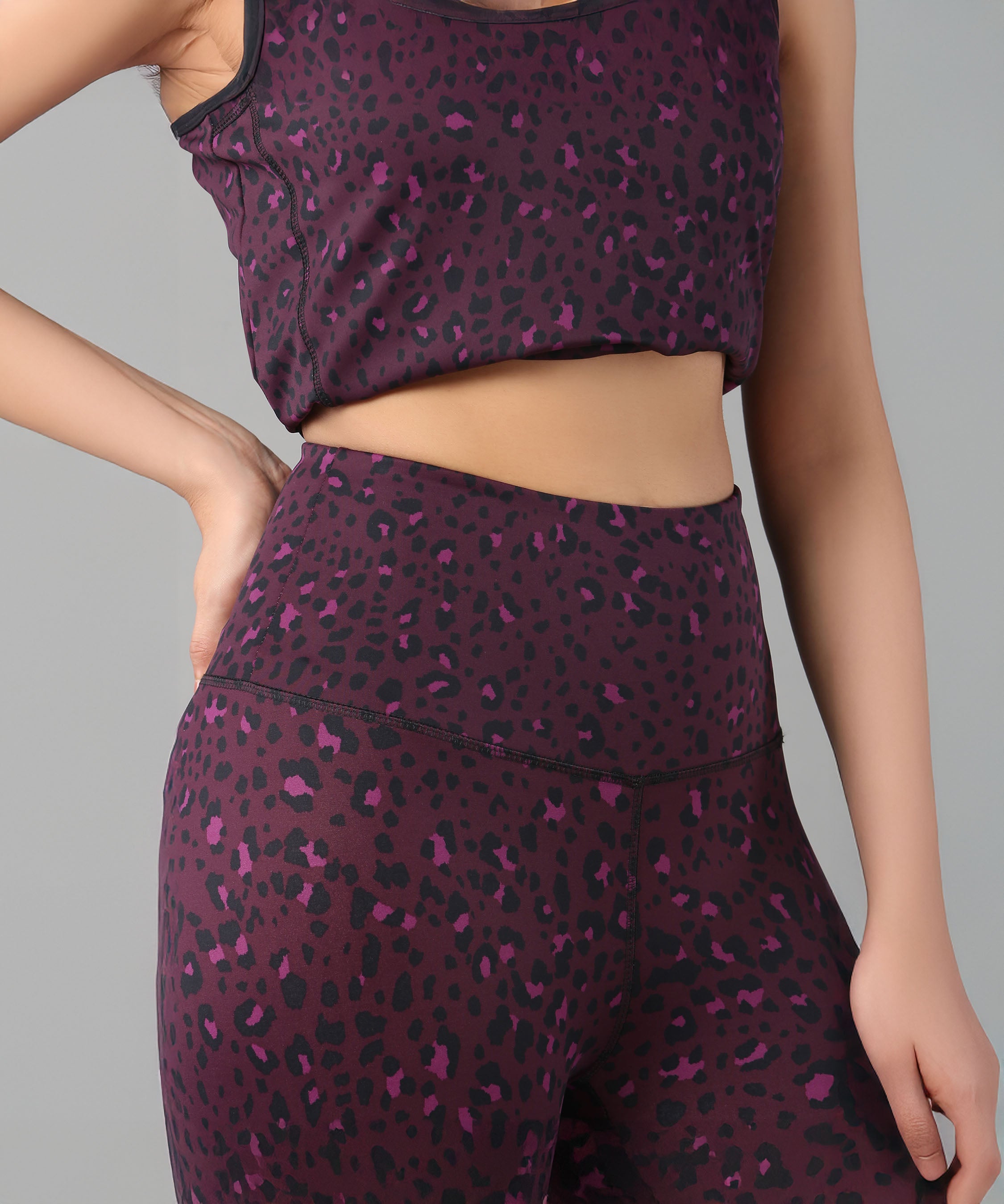 Woman in Pink Animal Print Leggings and matching top, hand on her hip, posing against a gray background.