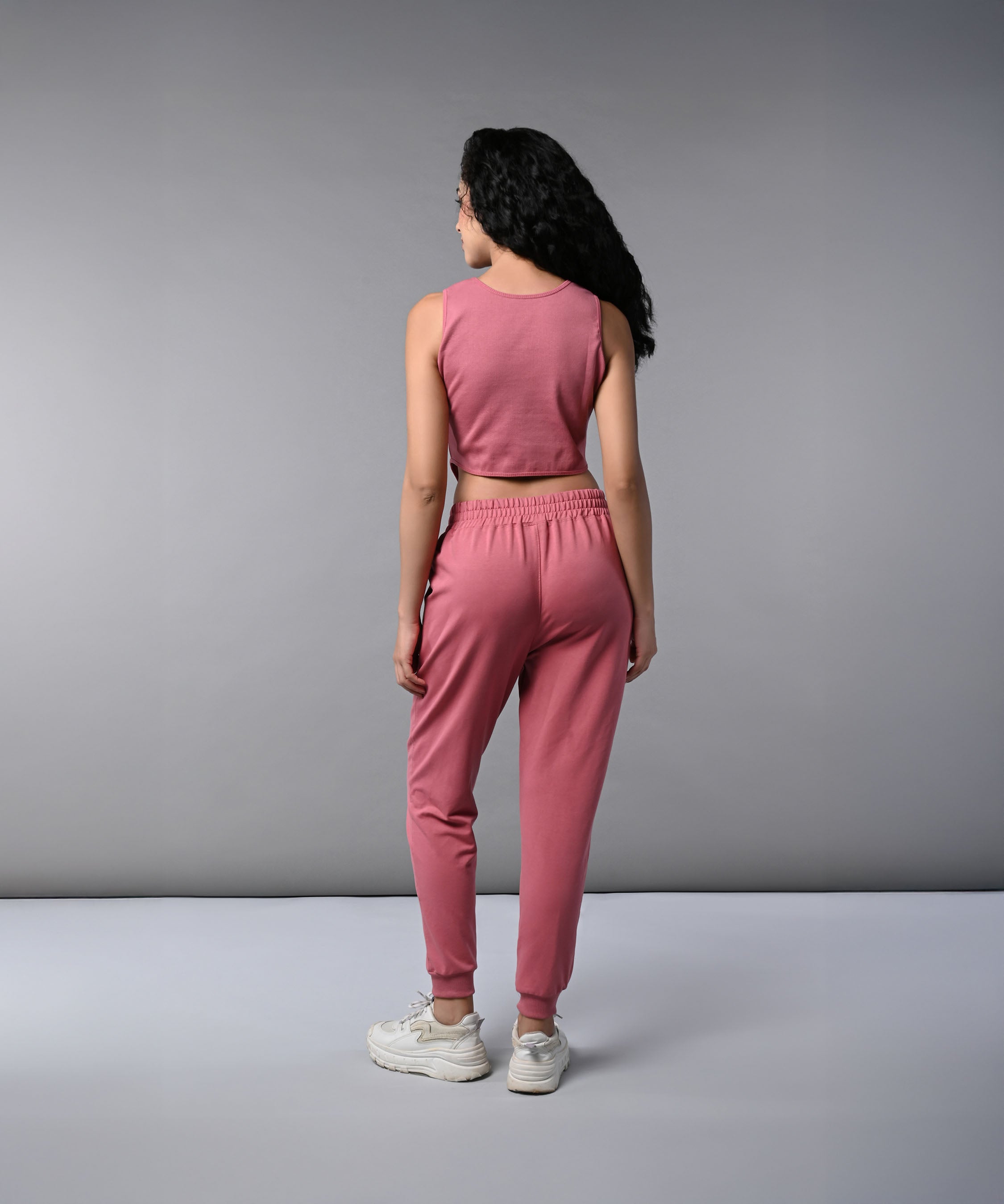Woman with long dark hair wearing a Pink Corset Crop-Top with Joggers co-ord set, featuring a sleeveless top and joggers, facing away in white sneakers.