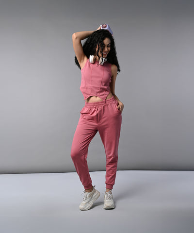 Woman wears a Pink Corset Crop-Top with Joggers, paired with headphones, posing confidently against a gray background.