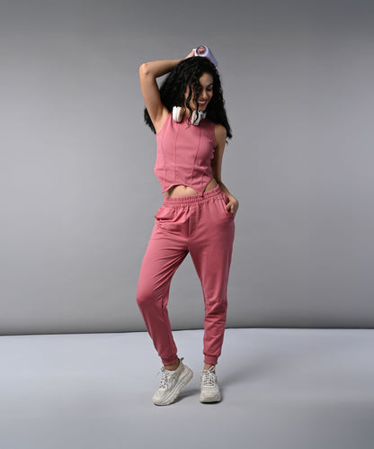 Woman wears a Pink Corset Crop-Top with Joggers, paired with headphones, posing confidently against a gray background.