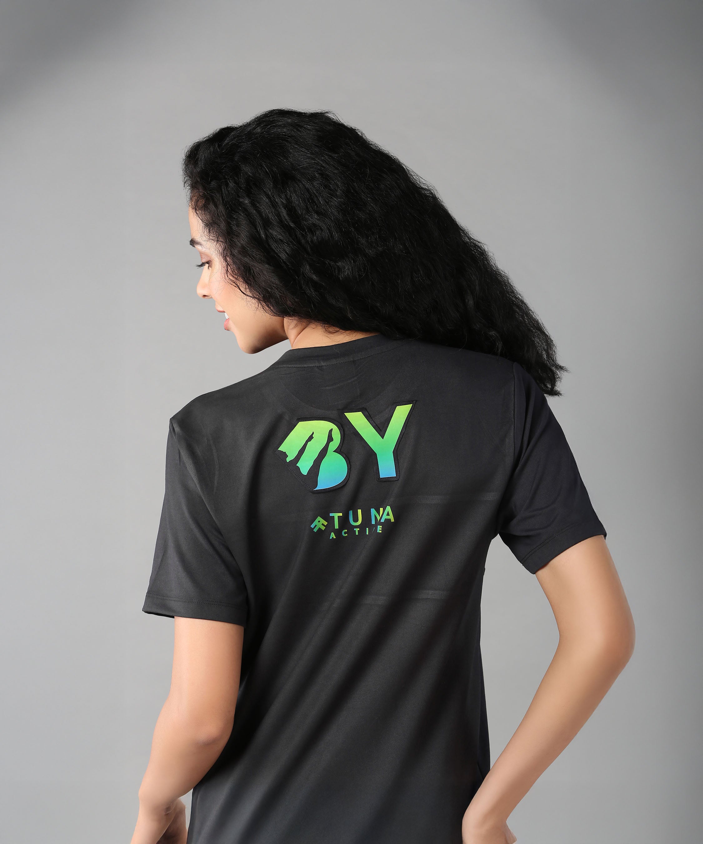 Woman with long black hair wears the Positive Body Image T Shirt, a black basic tee with half sleeves and a green "BY" and "Tuna Active" logo on the back, promoting positive body image.