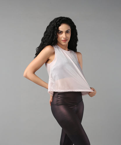 A woman with long curly hair poses against a gray background wearing the Powder Pink Sheer Top and shiny leggings.