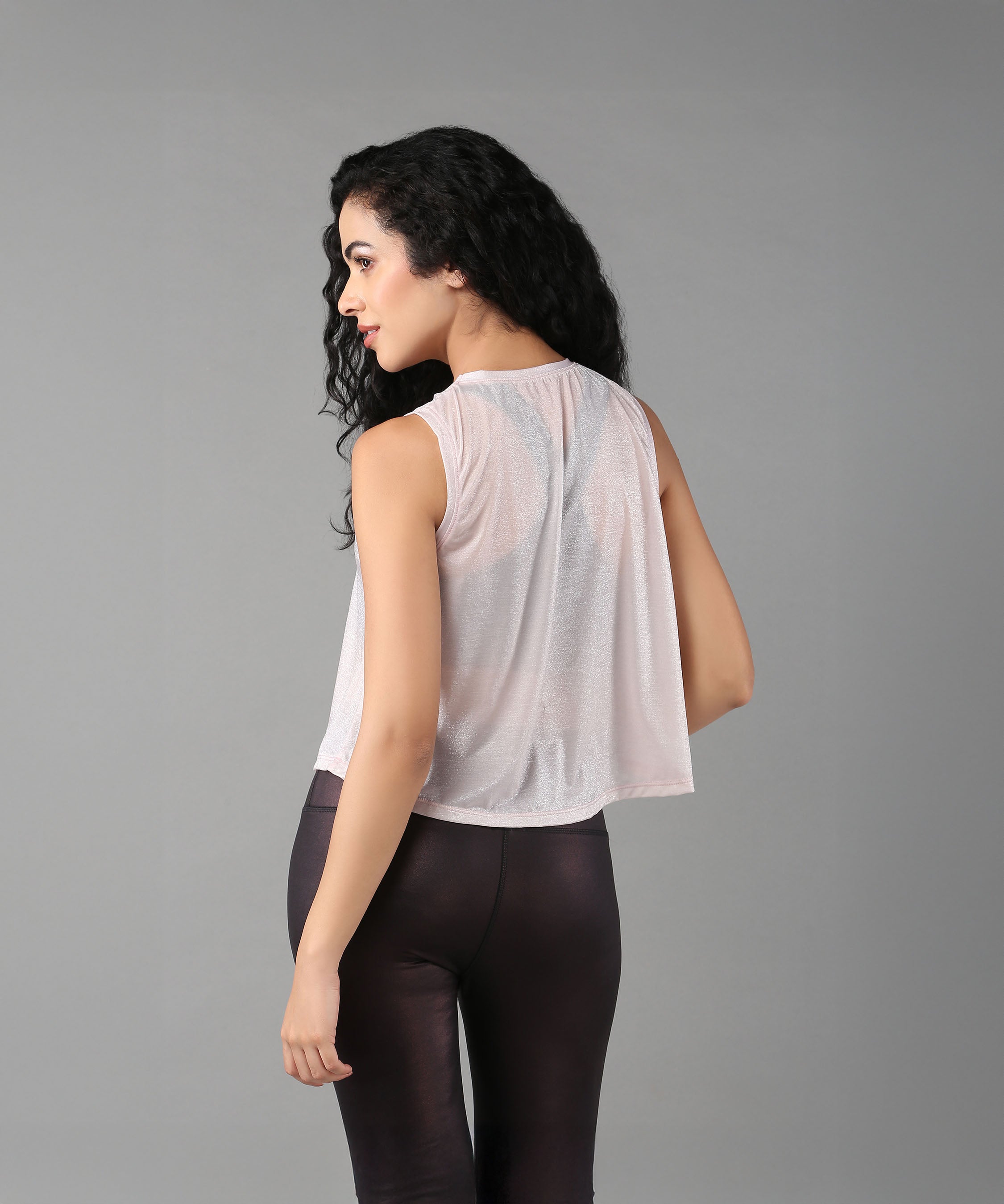Woman with long curly hair poses against a gray background, wearing the Powder Pink Sheer Top and black pants.