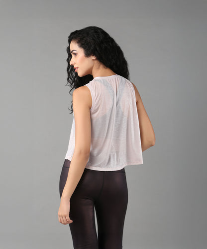 Woman with long curly hair poses against a gray background, wearing the Powder Pink Sheer Top and black pants.