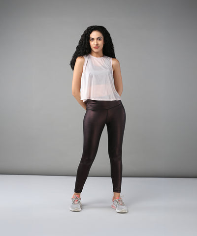 A woman with curly hair models the Powder Pink Sheer Top and shiny black leggings against a plain gray background.