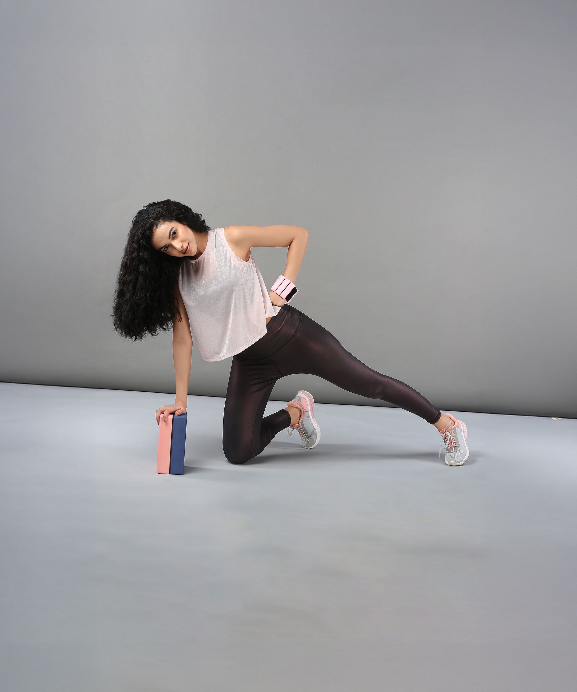 Woman wearing the Powder Pink Sheer Top balances on one knee with a yoga block, set against a plain gray background.