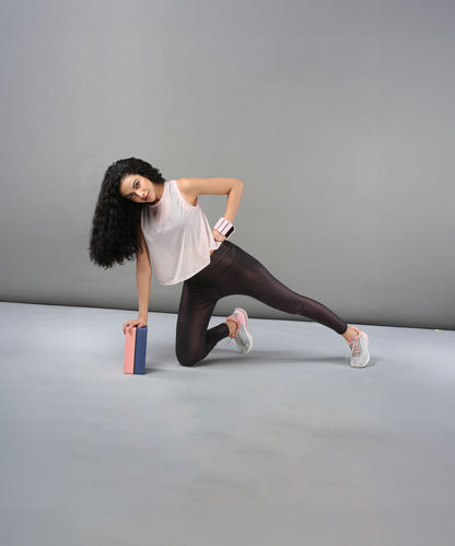Woman wearing the Powder Pink Sheer Top balances on one knee with a yoga block, set against a plain gray background.