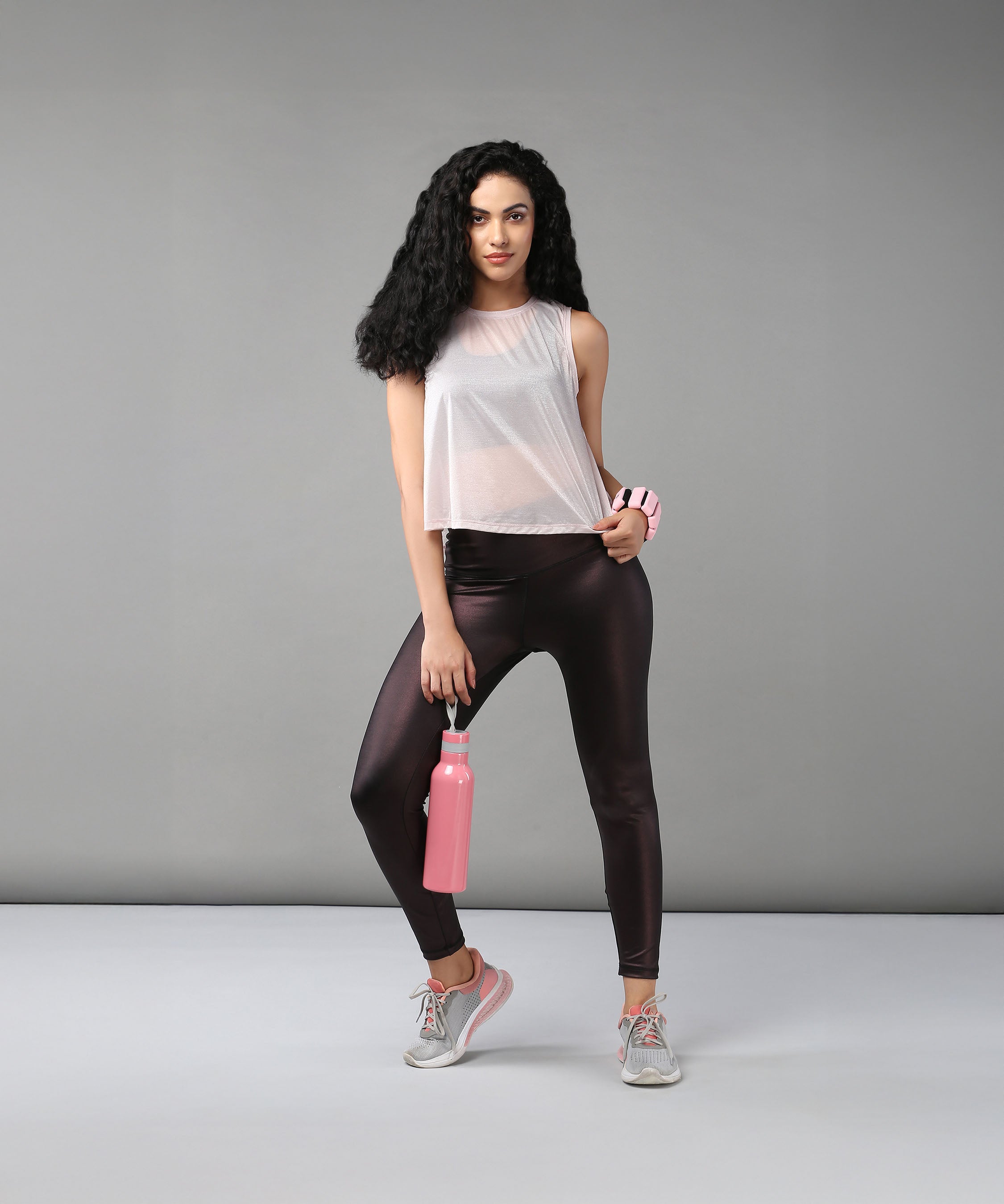 Woman wearing the Powder Pink Sheer Top and workout clothes holds a pink water bottle, standing against a plain gray background.