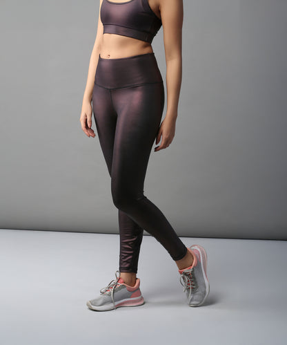 Woman in a metallic sports bra, Radiant Maroon Shimmer Leggings, and gray sneakers stands against a plain background.