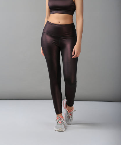A woman in high-waisted Radiant Maroon Shimmer Leggings and gray sneakers stands against a plain gray background.