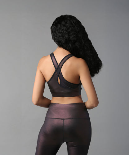 Woman with long black hair models the Radiant Maroon Shimmer Sports Bra and metallic workout attire, facing away against a plain gray background.