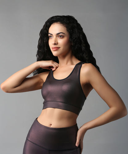 A woman with long curly hair wears the Radiant Maroon Shimmer Sports Bra, posing against a gray background.
