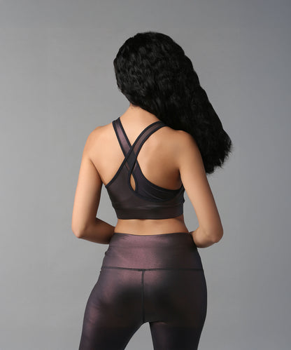 Woman wearing the Radiant Maroon Shimmer Sports Bra, a high-support, shiny workout top, seen from behind against a plain gray background.