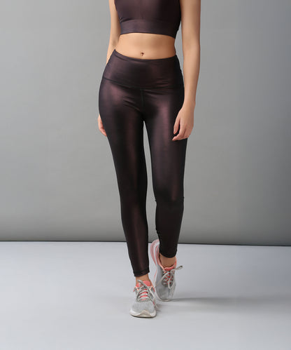 A woman showcases the Radiant Maroon Shimmer Work out Ensemble—dark maroon shimmer leggings and a matching crop top with a cross body racerback—styled with gray sneakers against a plain background.