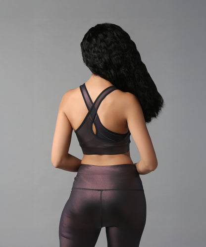 A woman in the Radiant Maroon Shimmer Work out Ensemble with a cross body racerback design is pictured from behind, her long wavy hair visible against a plain background.