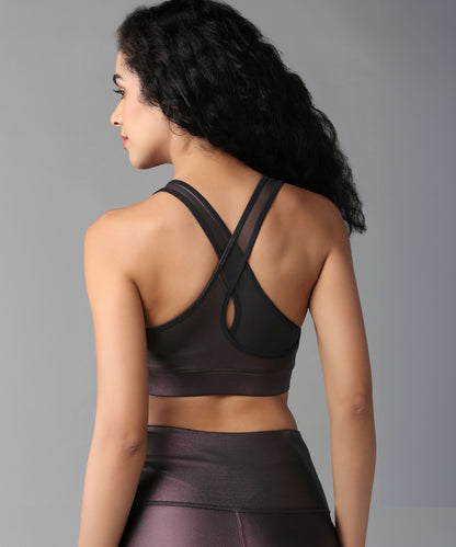 A woman with curly hair models the Radiant Maroon Shimmer Workout Ensemble—sports bra and leggings—in shiny fabric, shown from the back against a gray background.