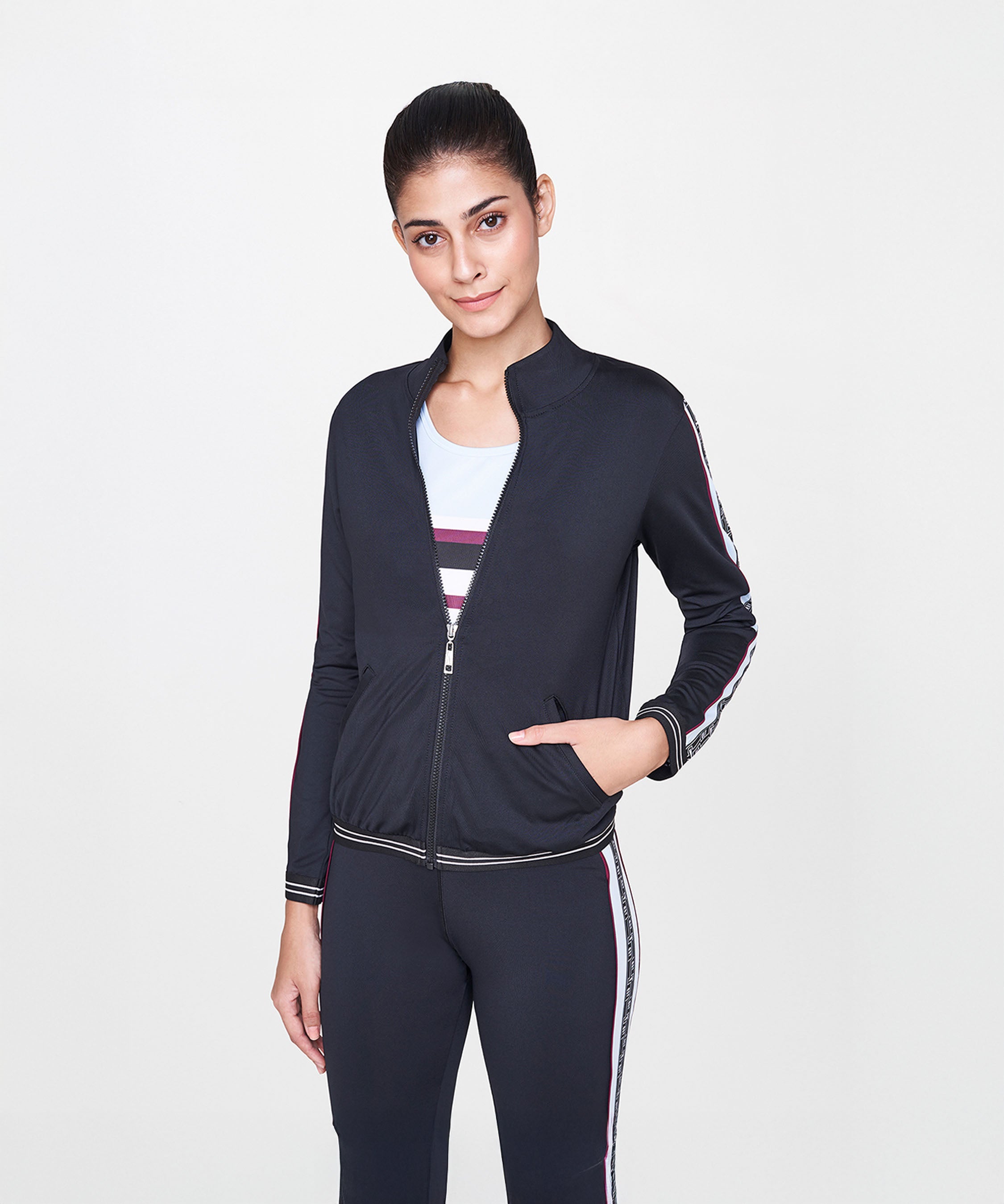 Woman wearing the Black Jacket With Track Pants set, featuring a fitted black jacket with striped accents and matching polyester track pants, smiling against a plain background.