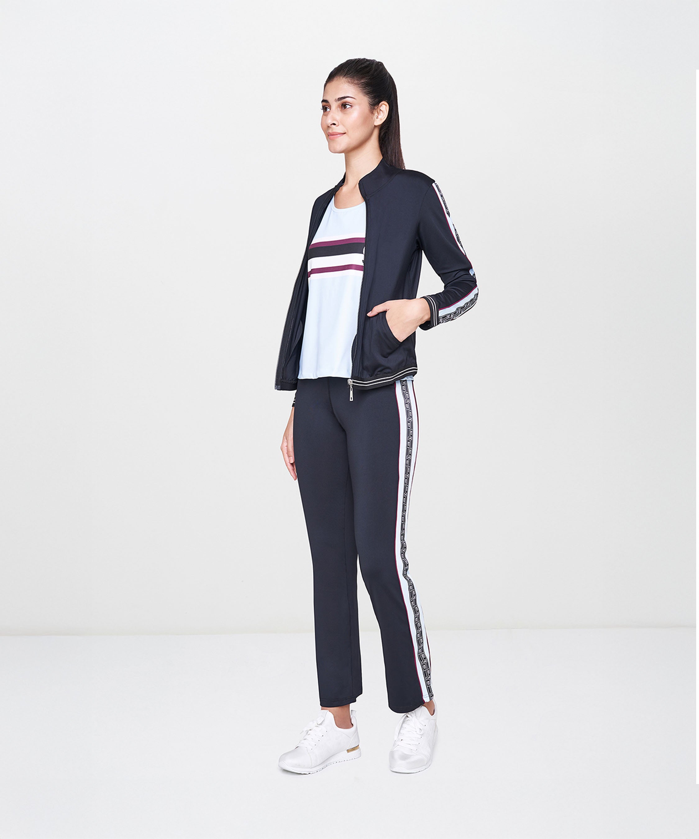 Woman wearing the Black Jacket With Track Pants set, featuring a fitted black jacket, polyester track pants, white top, and white sneakers, standing sideways.