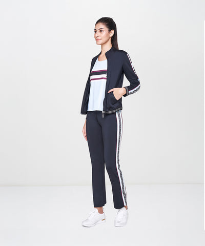 Woman wearing the Black Jacket With Track Pants set, featuring a fitted black jacket, polyester track pants, white top, and white sneakers, standing sideways.