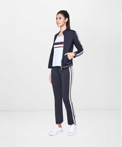 Woman wearing the Black Jacket With Track Pants set, featuring a fitted black jacket, polyester track pants, white top, and white sneakers, standing sideways.