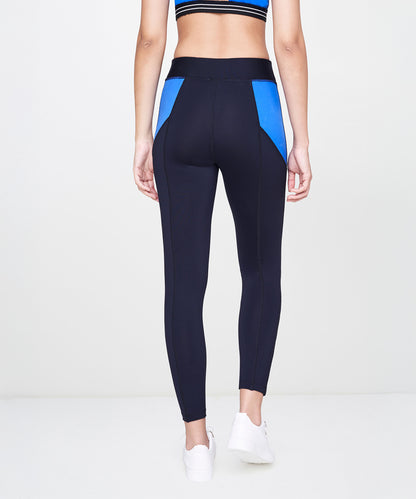 Woman in Indigo Leggings with black panels, white sneakers, and a striped sports bra, pictured from the back.