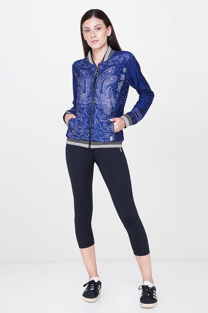 A woman stands confidently against a plain white background, wearing Black Leggings paired with a blue patterned jacket and classic white sneakers—a true wardrobe essential.