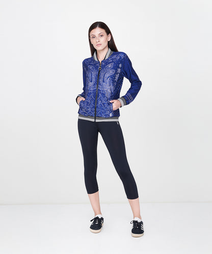 Woman wearing black leggings, a blue patterned jacket, and sneakers, standing against a white background.