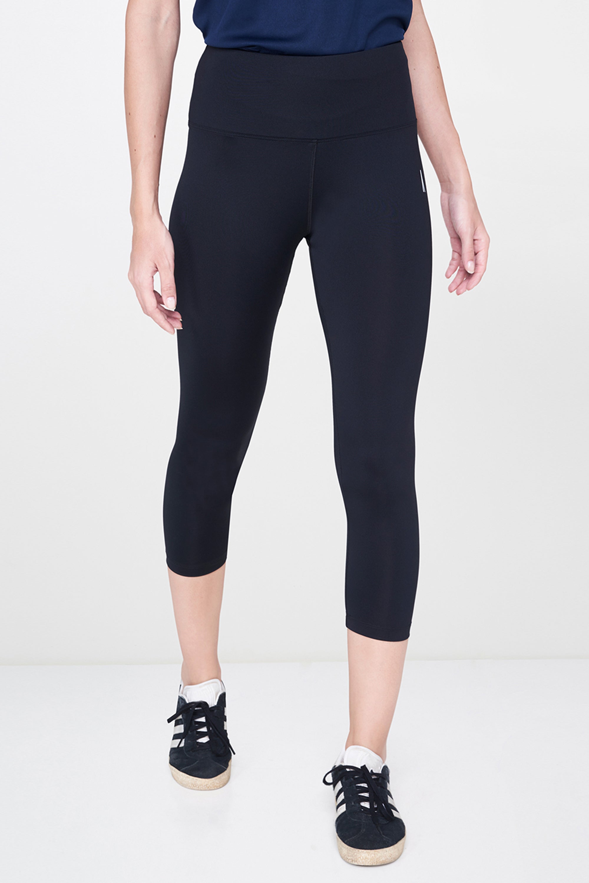 Wearing Black Leggings and white sneakers with white soles paired with a navy top, this must-have look stands out against a white background.