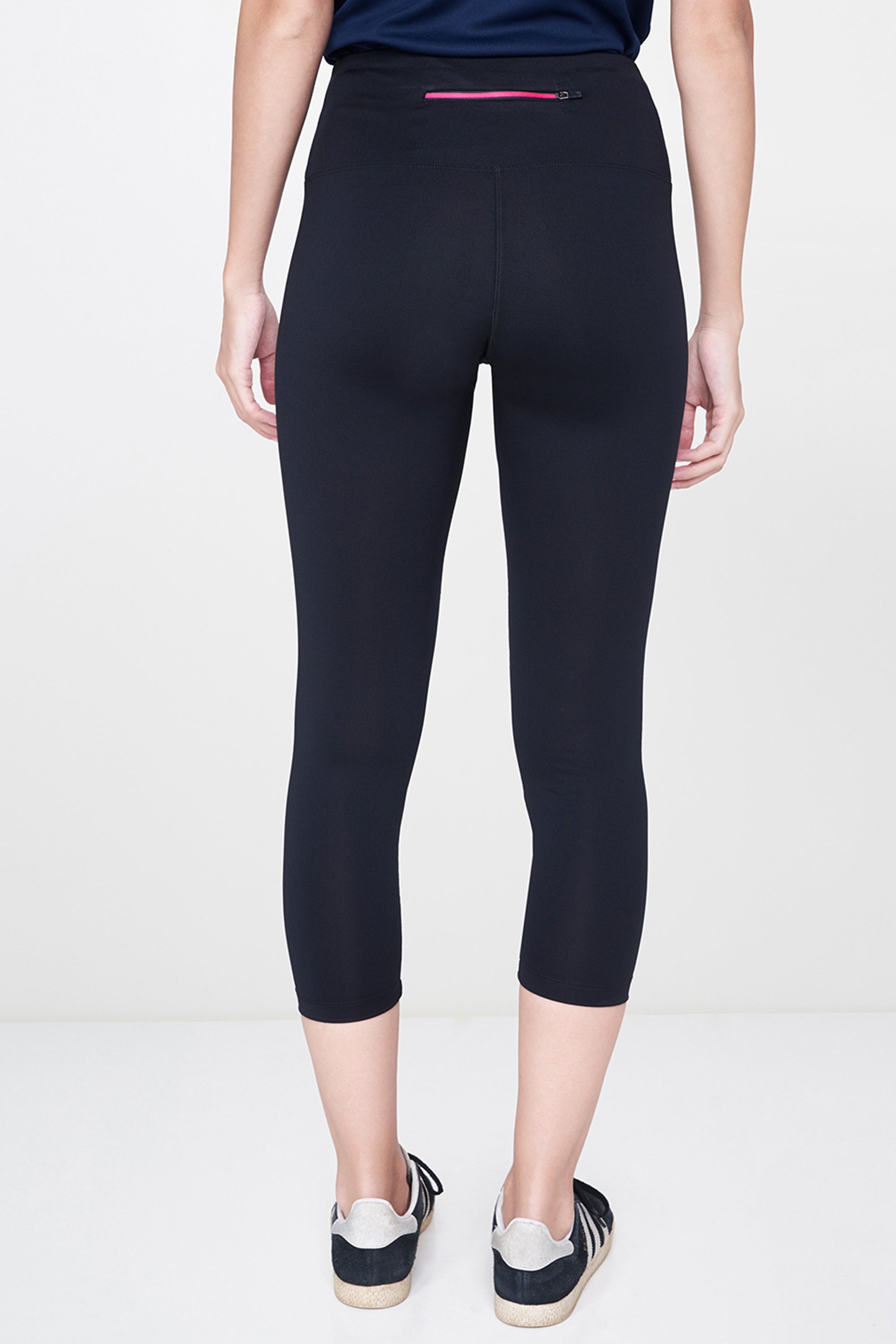 Someone is seen from the back wearing Black Leggings and classic white sneakers against a plain background—an effortless wardrobe essential.