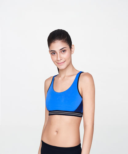 A woman with dark hair smiles in a Blue Sports Bra against a plain white background, ready for her workout in stylish activewear.