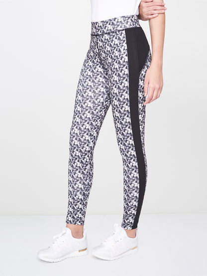 A woman stands sideways in White Printed Leggings featuring a stretchy polyester-spandex blend, black side panels, and white sneakers.