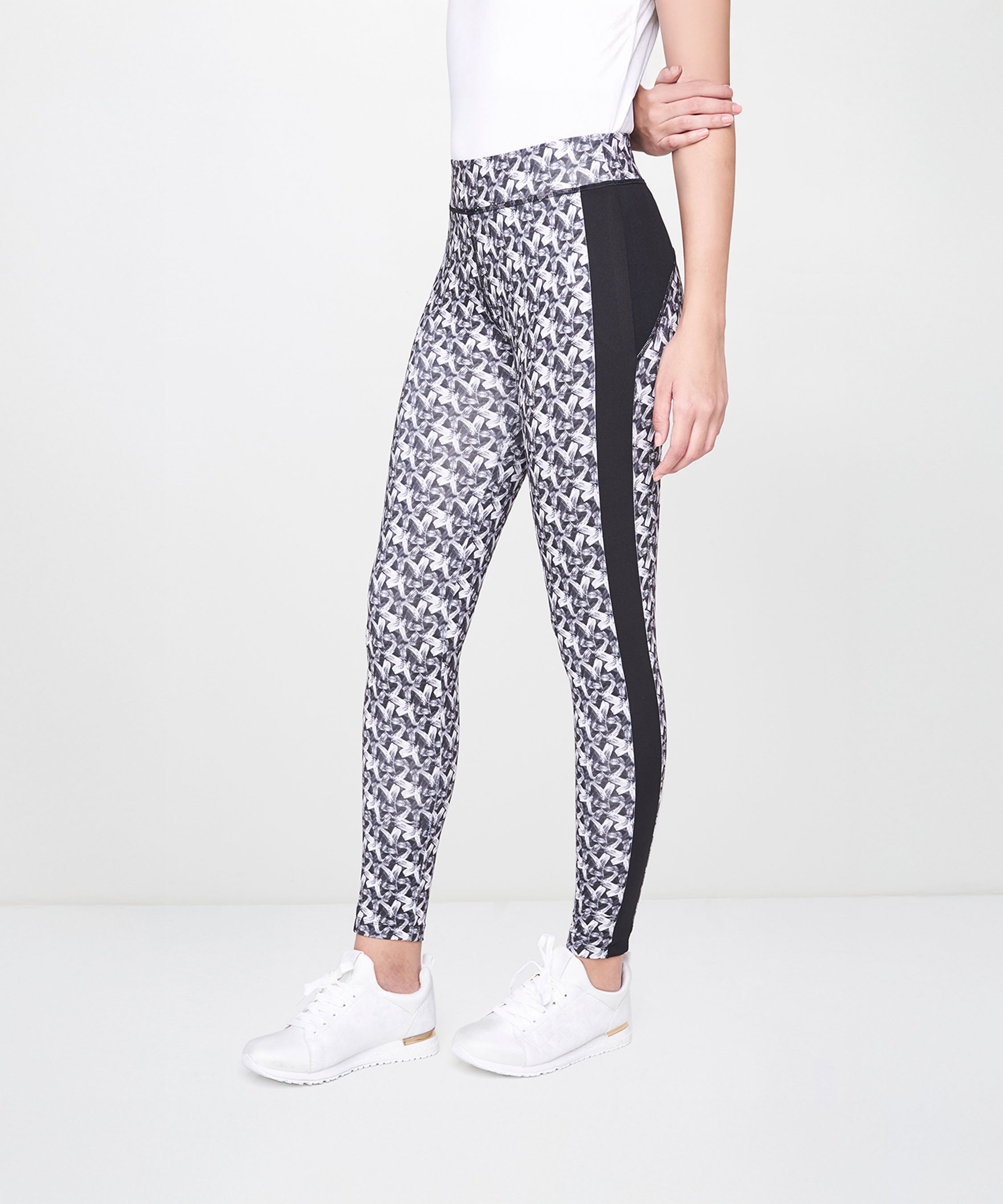 Woman stands sideways wearing White Printed Leggings with black side panels, a white shirt, and white sneakers. The leggings are breathable and patterned, offering both style and comfort.