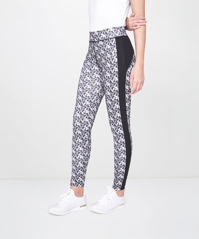 Woman stands sideways wearing White Printed Leggings with black side panels, a white shirt, and white sneakers. The leggings are breathable and patterned, offering both style and comfort.