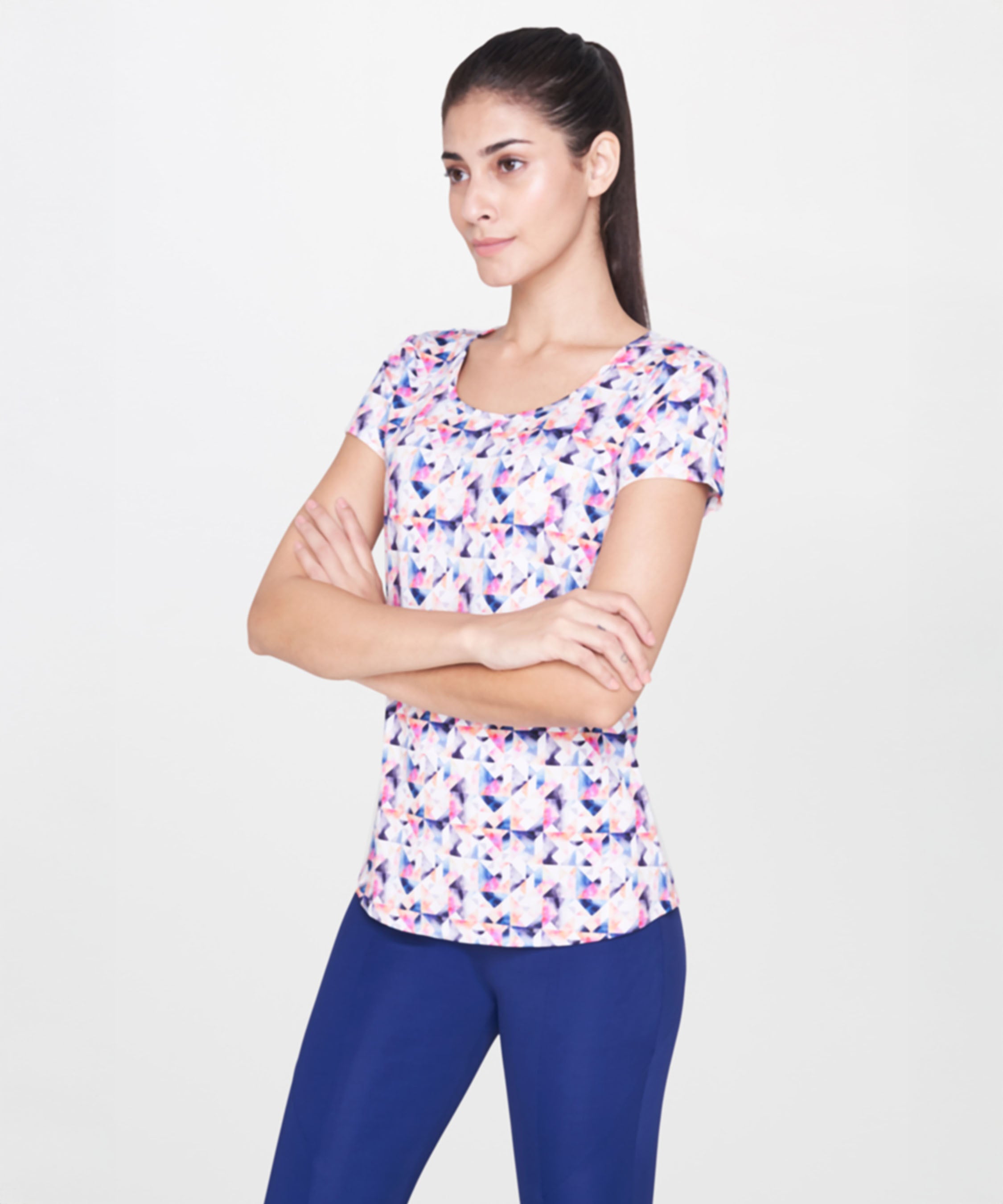 Woman wearing a White Multicolour Printed Top and blue pants stands with arms crossed, looking to the side.
