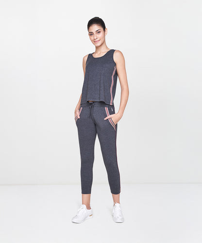 Woman wearing a Grey Sleeveless Tank Top and charcoal jogger pants with pink stripes, standing and smiling. SS19ATHAND34.