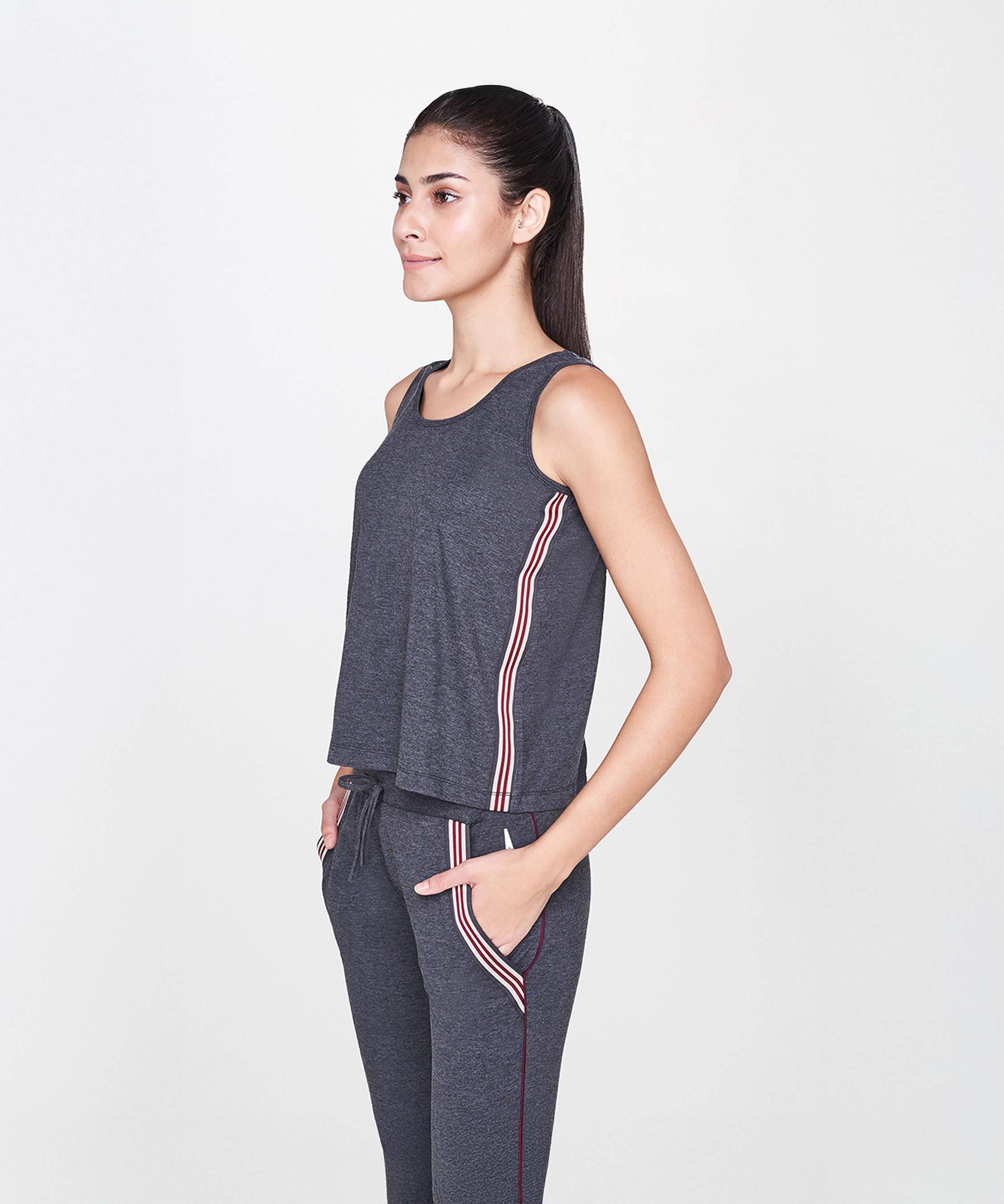 Woman in a Grey Sleeveless Tank Top and matching pants with side stripes, standing with hands in pockets.