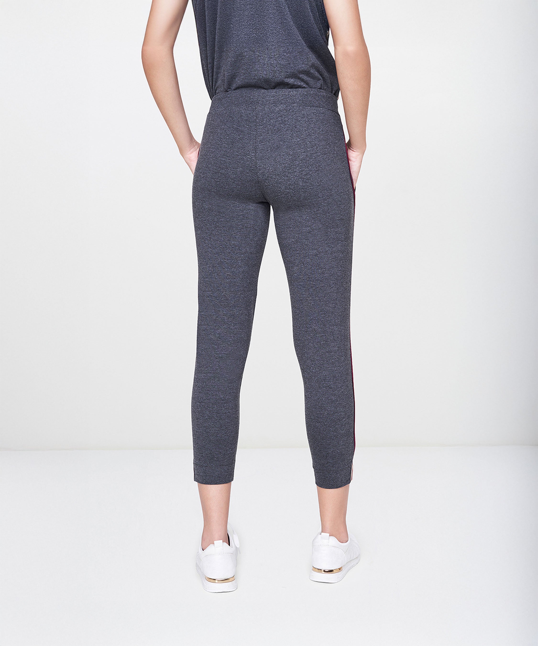 A person is wearing the Dark Grey Milange Tank Top With Joggers, paired with white sneakers and standing with hands behind their back.