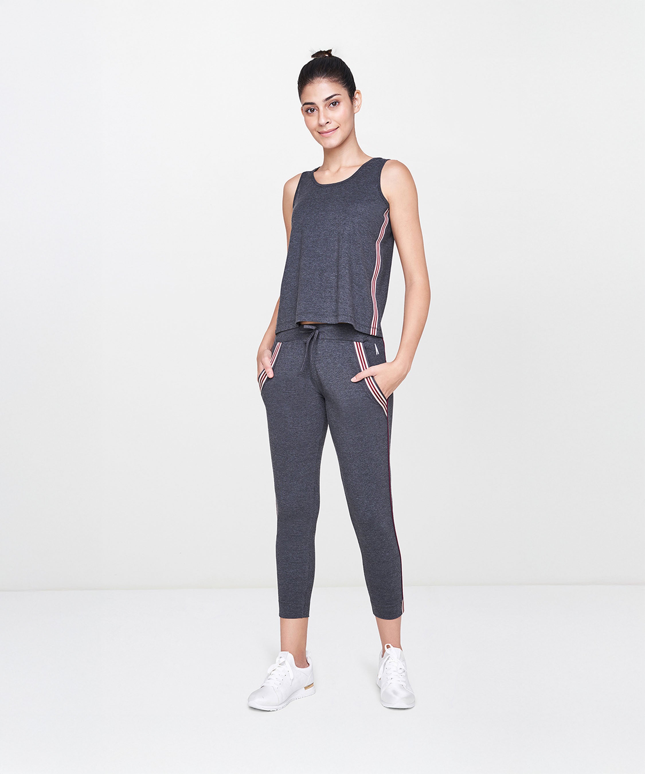 Woman wearing the Dark Grey Milange Tank Top With Joggers, smiling and standing in a white studio.