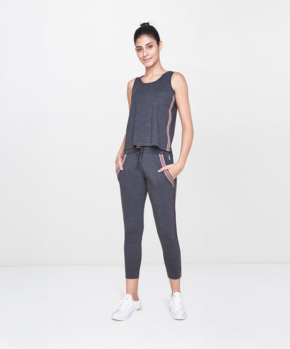 Woman wearing the Dark Grey Milange Tank Top With Joggers, smiling and standing in a white studio.