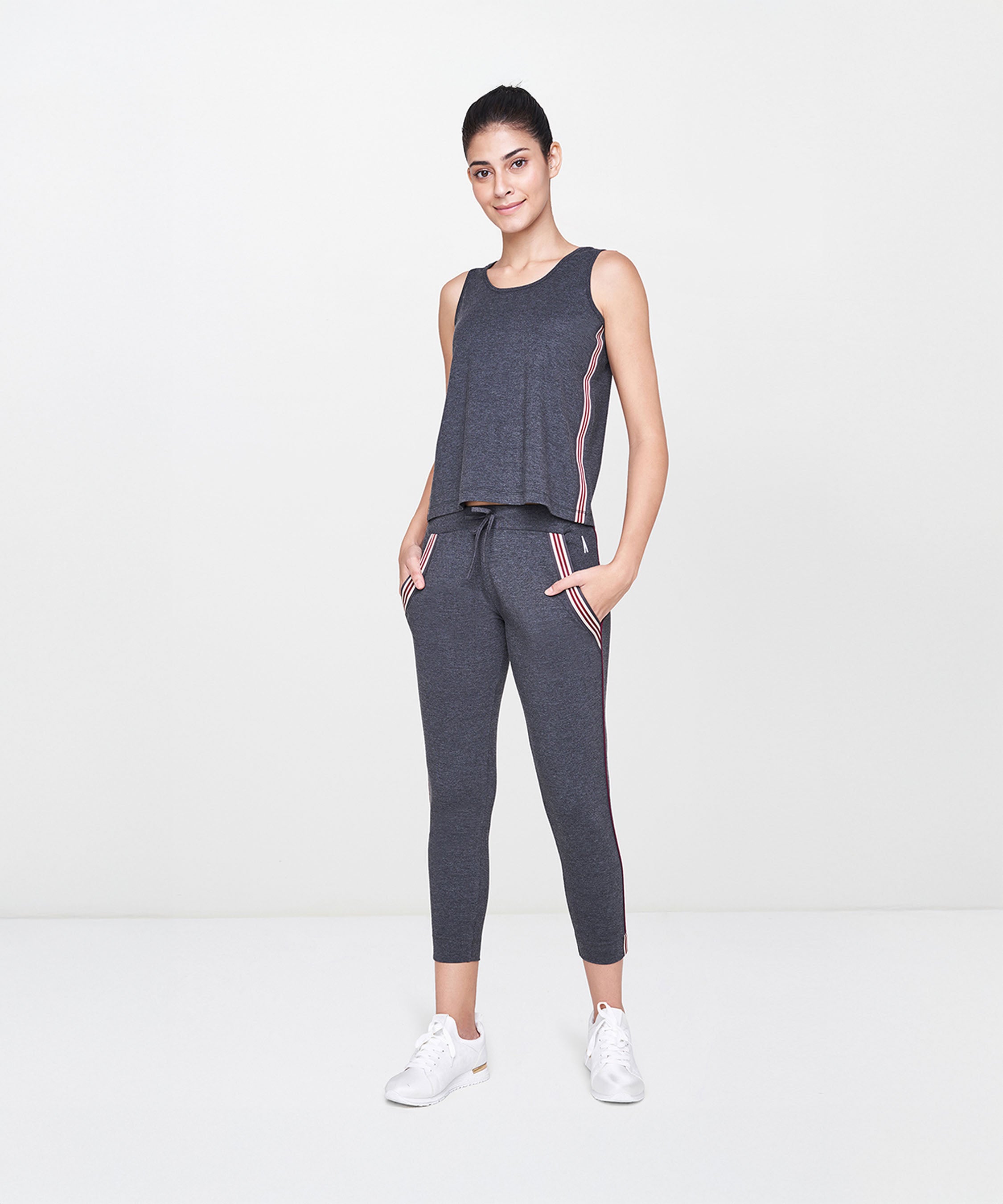 Woman wearing Grey Joggers With Pockets, paired with a dark gray sleeveless top and white sneakers, standing and smiling.