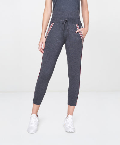 A person is wearing the Dark Grey Milange Tank Top With Joggers, featuring white and red side stripes, along with white sneakers, standing against a white background.