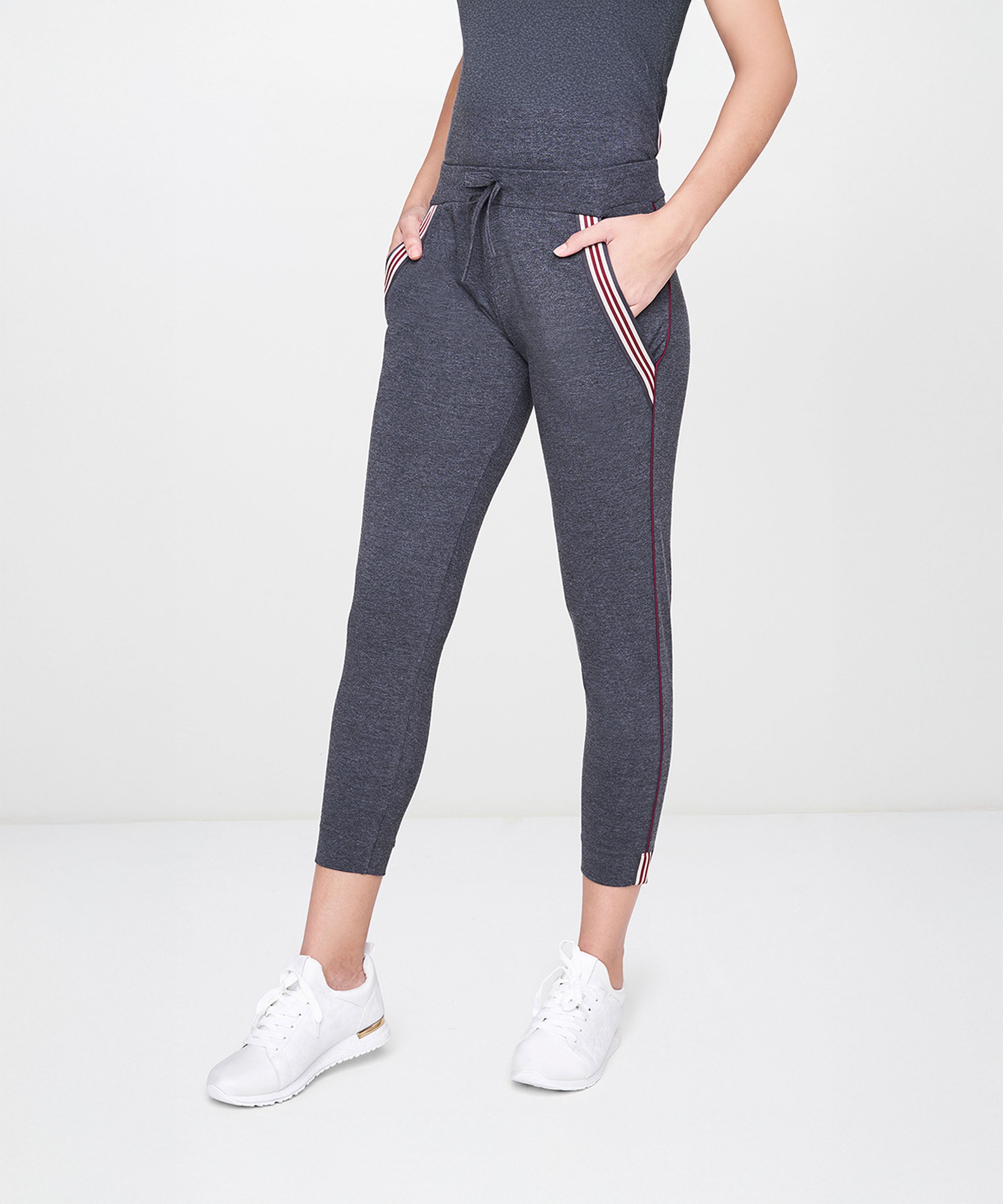 A woman stands with hands in pockets, wearing Grey Joggers With Pockets, white sneakers, and a dark top.