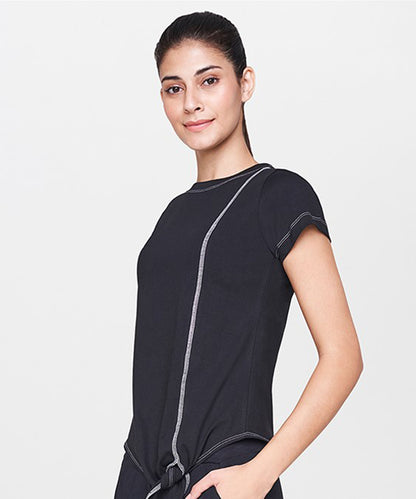 A smiling woman with dark hair in a ponytail wears the Black T-Shirt—a short-sleeved top featuring white stitching, making it an ideal staple for casual outfits.