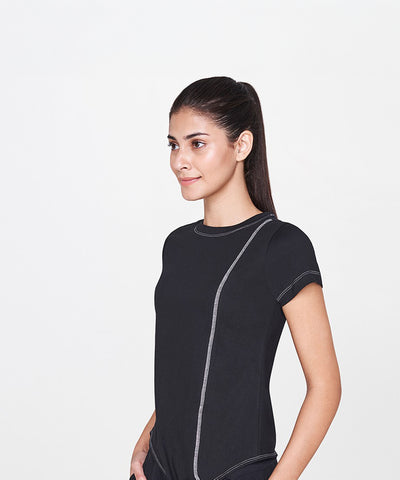 A woman with long dark hair in a ponytail wears the Black T-Shirt, a classic wardrobe staple, while standing against a plain white background.