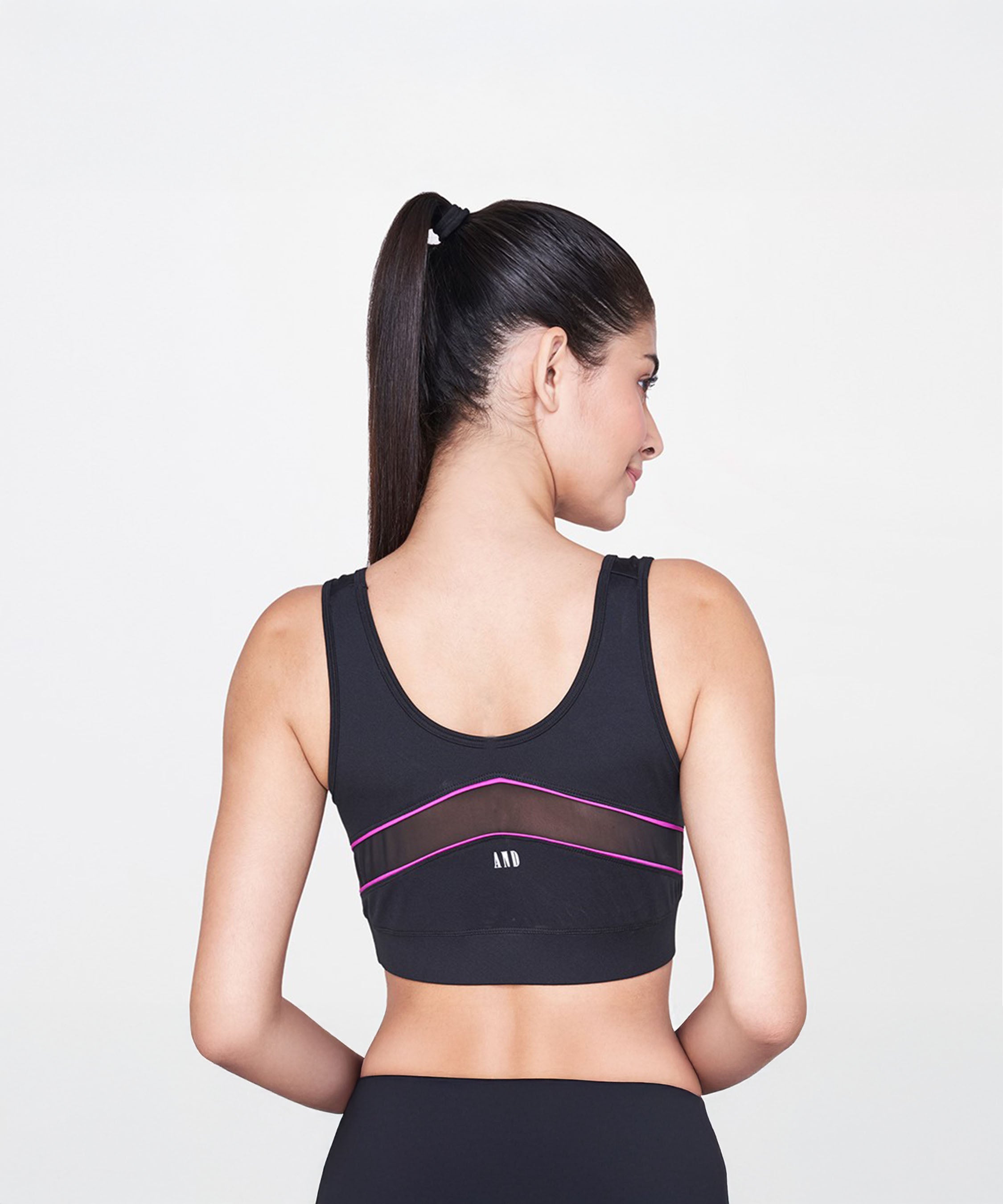 A woman with a ponytail models the Black and Pink Sports Bra, shown from the back against a white background.