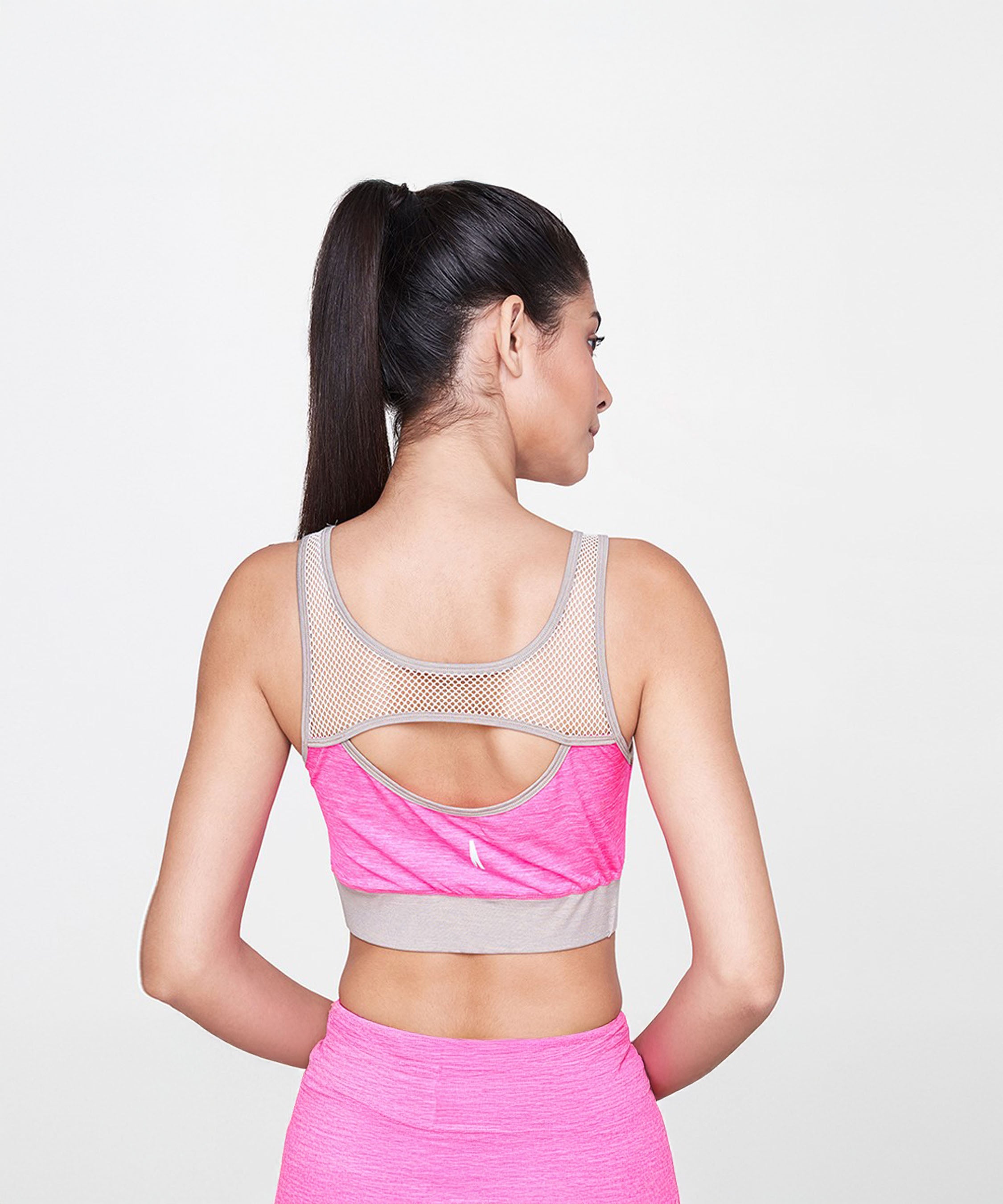 A woman with a ponytail wears the Pink Sports Netted Bra and matching leggings, activewear set, as she faces away from the camera.