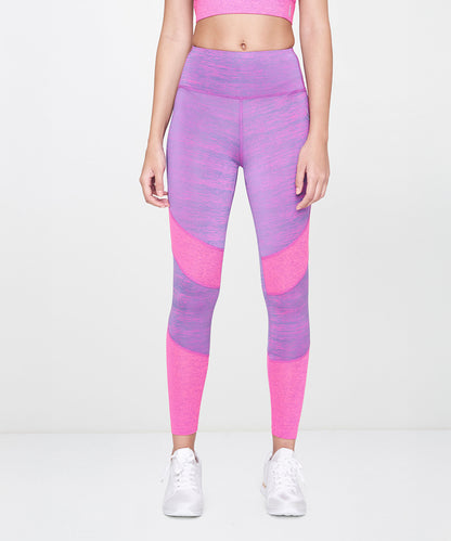 Woman wearing Pink Leggings, paired with a purple sports bra and white sneakers, standing against a plain background.